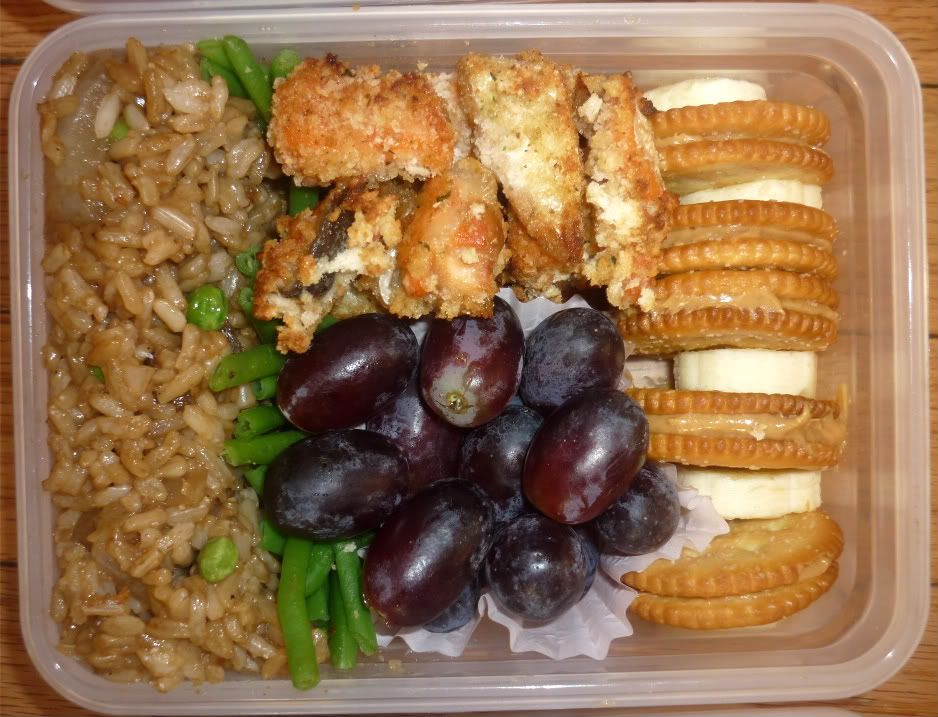 Bento box - Brown rice with soy sauce, onions, peas; Green beans; Baked steelhead salmon rainbow trout nuggets with panko bread crumbs; grapes in a muffin tin liner; peanut butter crackers with sliced bananas